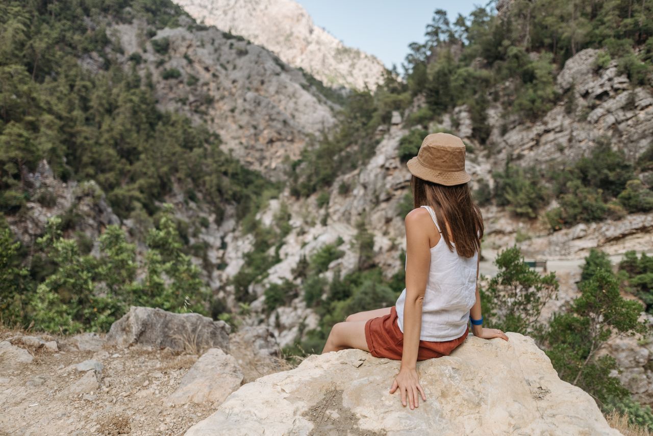 services-01 A woman sits on a rock enjoying a stunning mountain view outdoors.